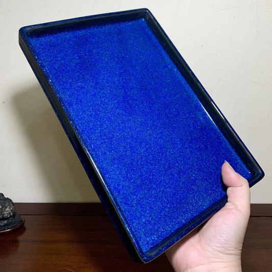 A hand holds a rectangular, glossy cobalt blue glazed tray with a slightly raised rim.