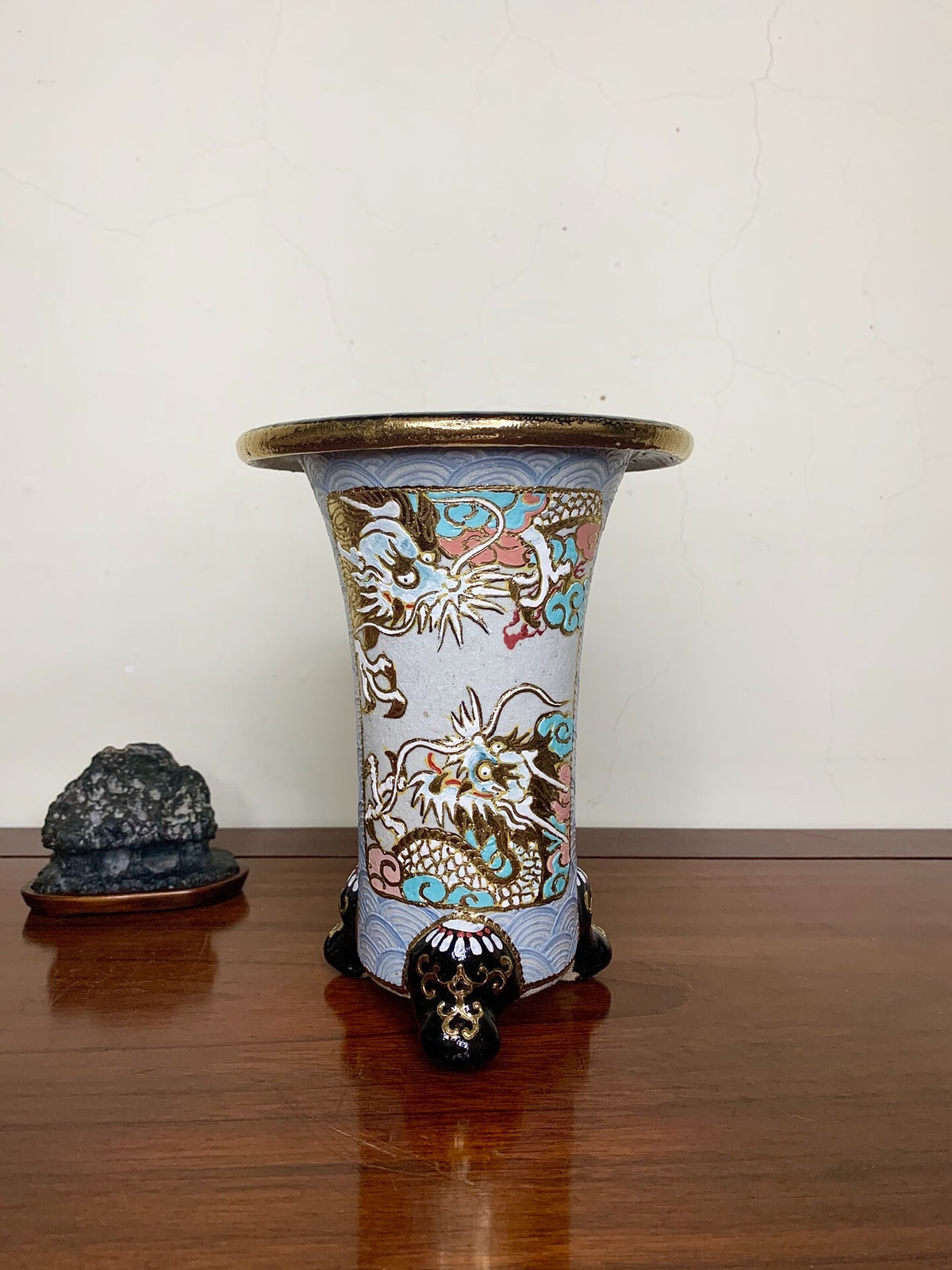 A tall, light blue glazed pot with gold and multi-colored dragons, standing on three black feet.