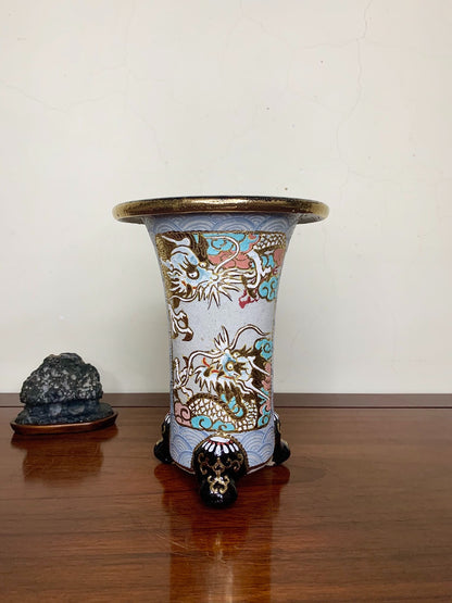 A tall, light blue glazed pot with gold and multi-colored dragons, standing on three black feet.