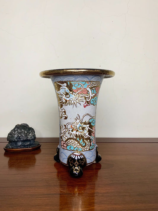 A tall, light blue glazed pot with gold and multi-colored dragons, standing on three black feet.