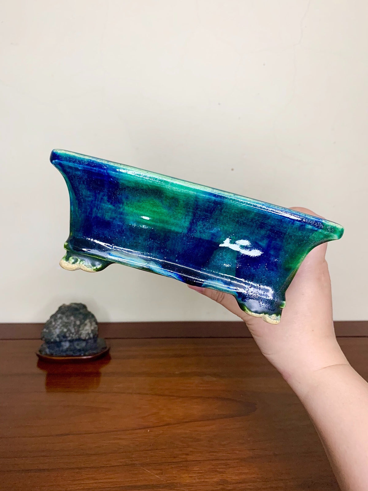 A hand holds a glossy, rectangular pot with a vibrant blue and green glaze.