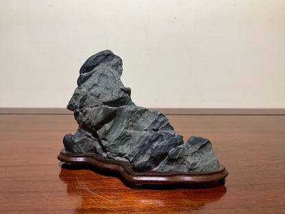 A dark grey, rough-textured rock with layered striations sits on a polished wooden base.