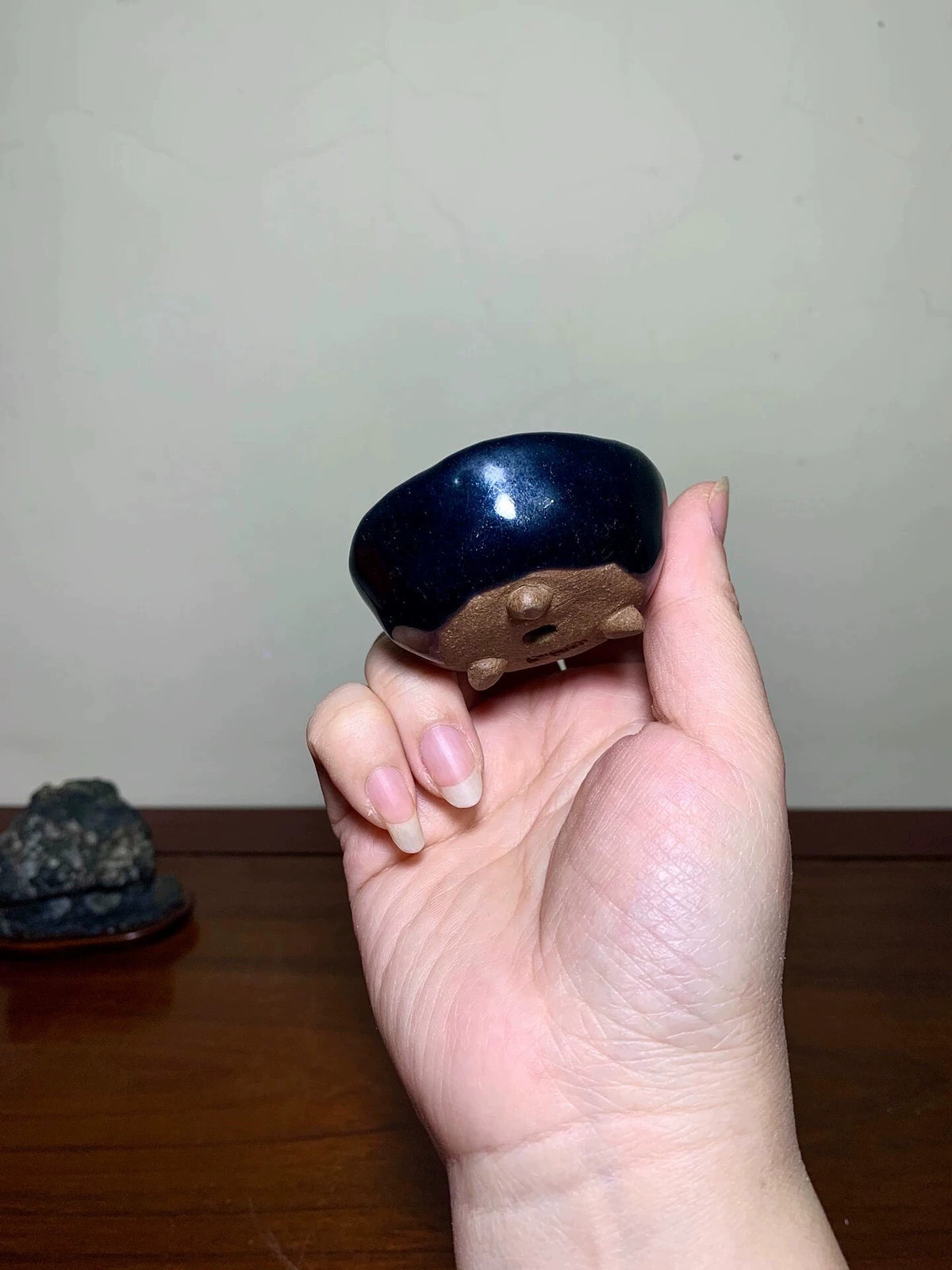 A hand holds a small, glossy dark blue ceramic pot with a brown unglazed base and three small feet.