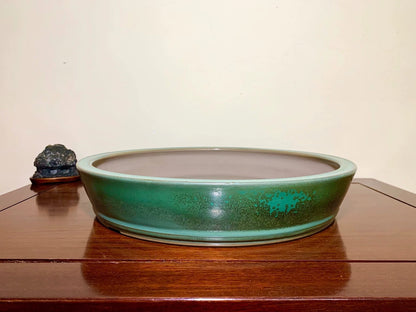 A low, wide ceramic pot with a glossy green glaze and speckled texture sits on a wooden surface.