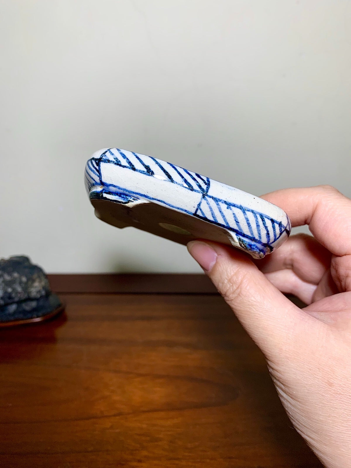 A hand holds a small, white ceramic pot with blue diagonal brushstroke patterns.