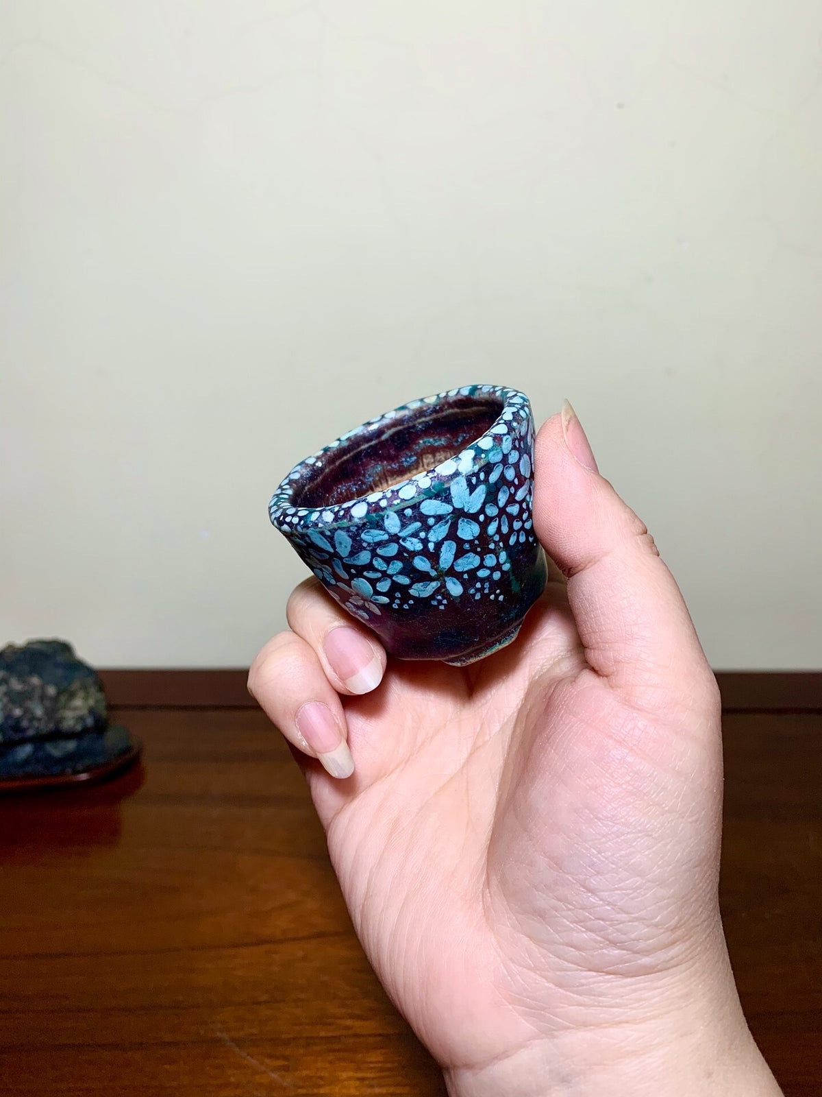A hand holds a small, glossy ceramic pot with a blue and black speckled glaze.
