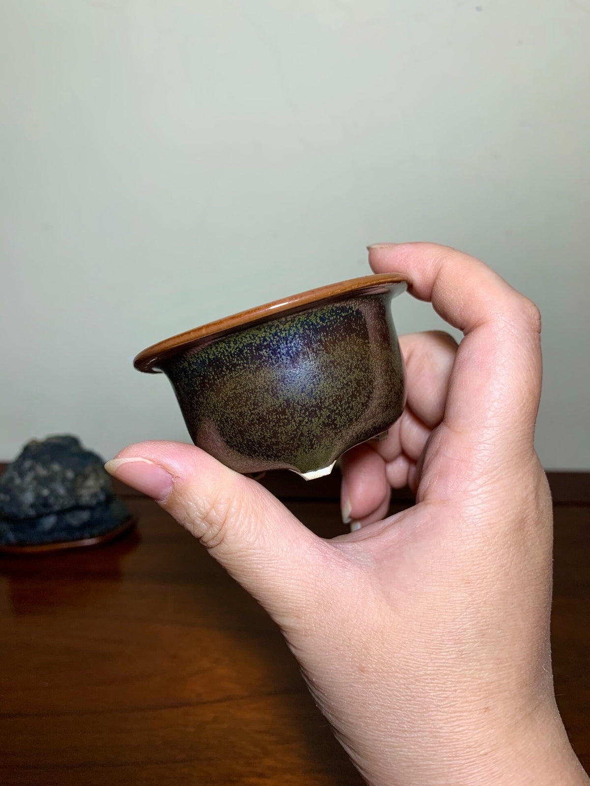 A hand holds a small, round, glazed ceramic pot with a mottled brown and blue glaze.