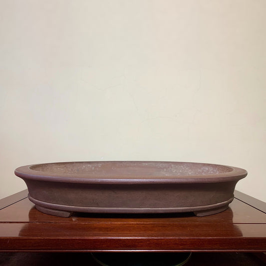 A low, oval, unglazed brown ceramic pot with a matte finish and subtle surface texture.