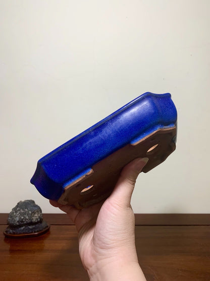 Hand holds a glossy cobalt blue glazed rectangular pot with brown unglazed rim and drainage holes.