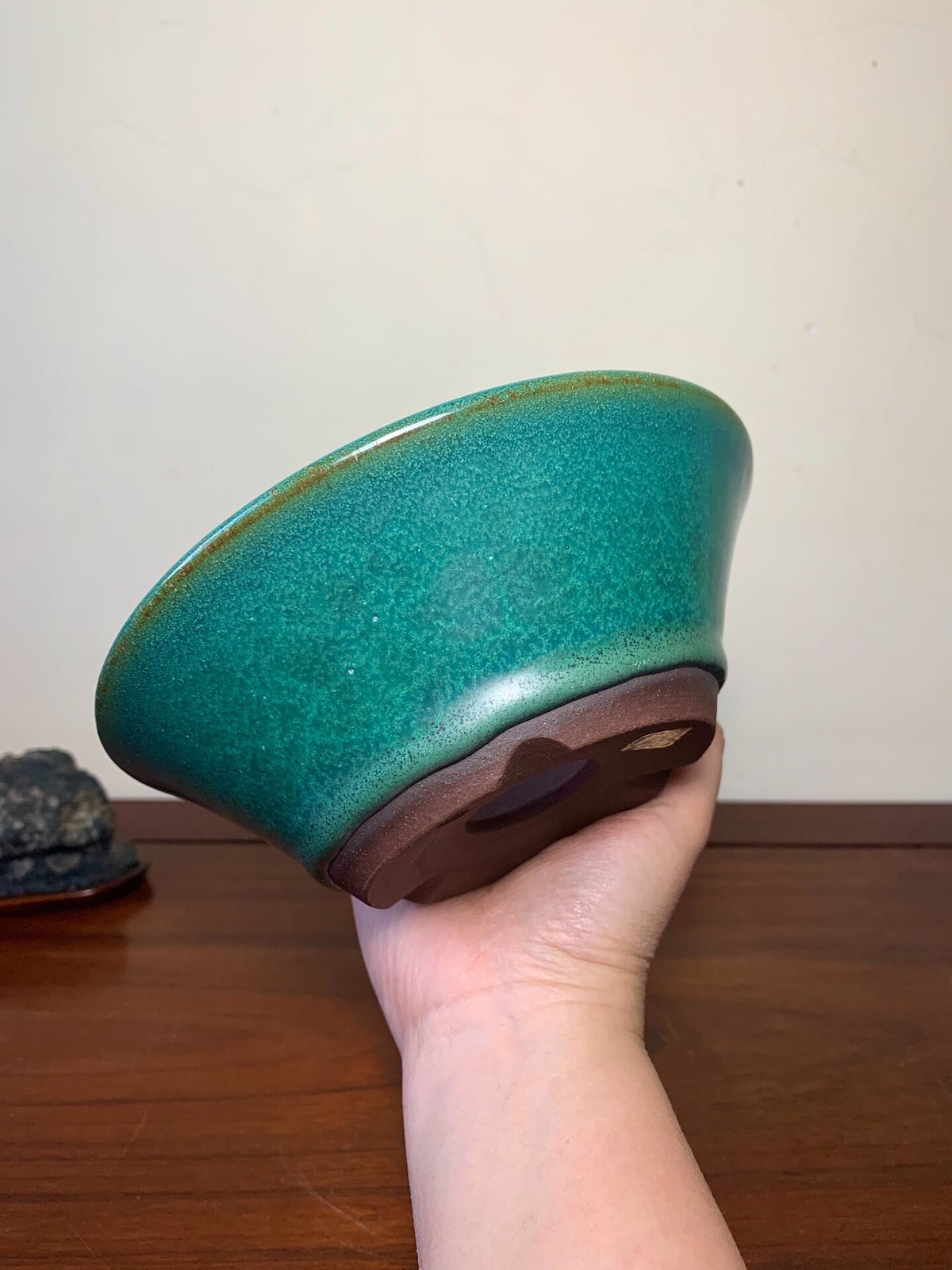 A hand holds a glossy teal glazed bowl with a brown unglazed base.