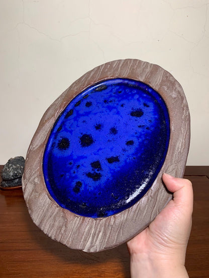 Hand holds oval pot with glossy cobalt blue glazed interior and textured brown rim.