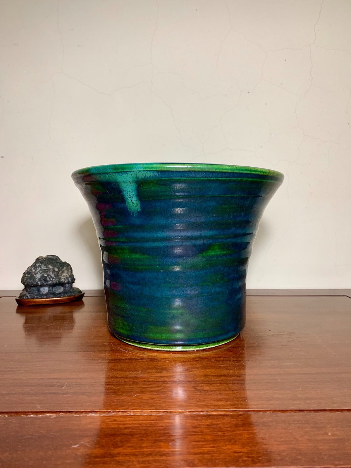 A glossy, flared ceramic pot with swirling green and blue glaze sits on a wooden surface.