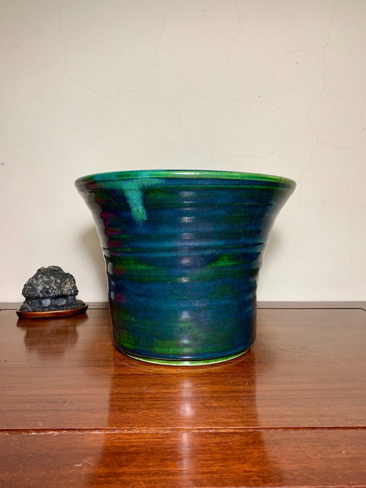 A glossy, flared ceramic pot with swirling green and blue glaze sits on a wooden surface.
