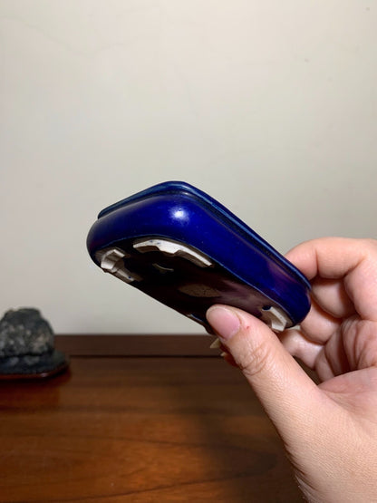 Hand holds a glossy cobalt blue ceramic pot with white glaze drips at base.