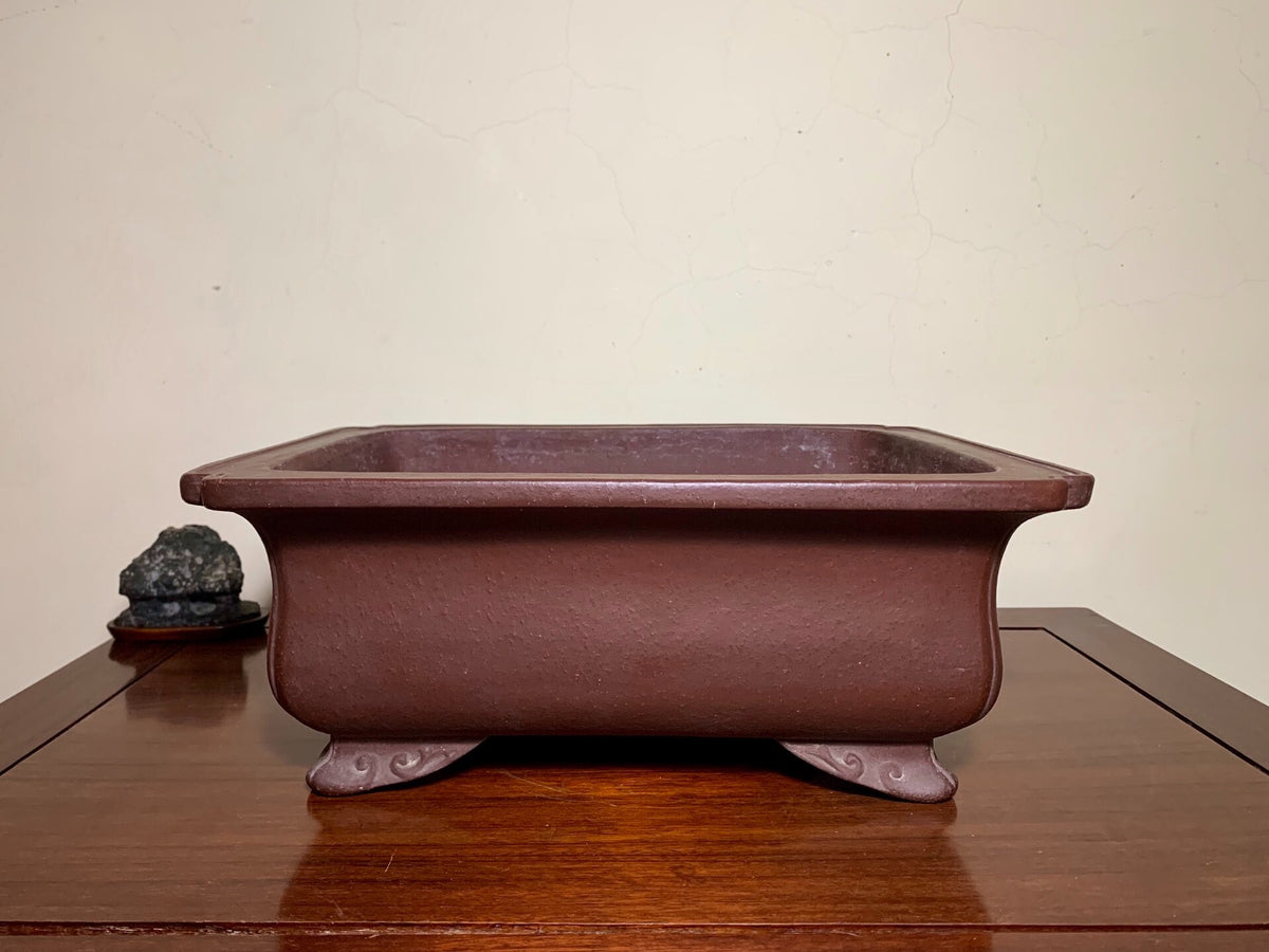 Rectangular brown unglazed ceramic pot with four footed supports, matte finish.