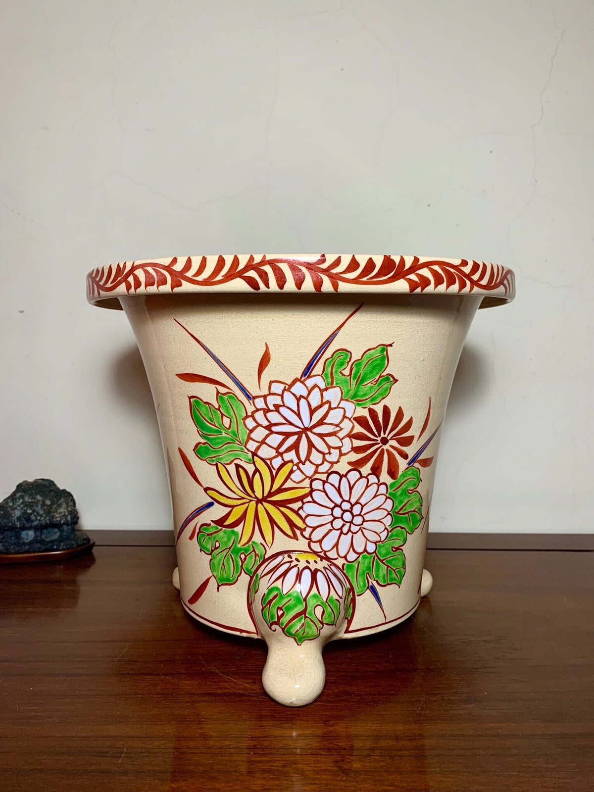 Cream glazed pot with red rim and painted floral design on three feet.