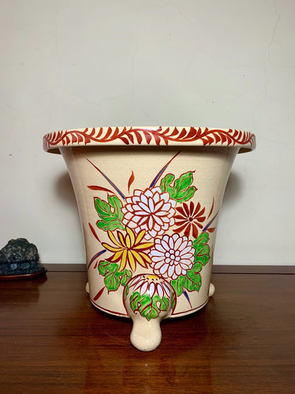 Cream glazed pot with red rim and painted floral design on three feet.