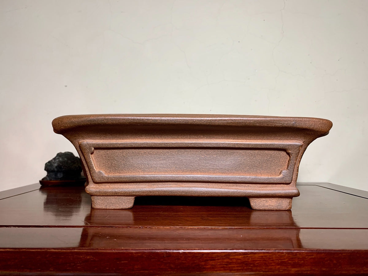 A brown, rectangular, unglazed ceramic pot with a low rim and footed base.
