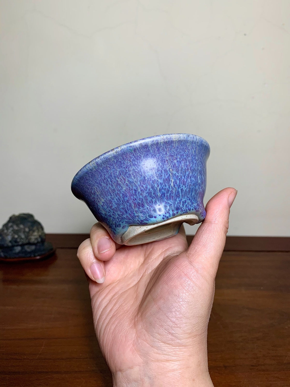 A hand holds a small, blue-glazed ceramic bowl with a speckled, glossy surface.