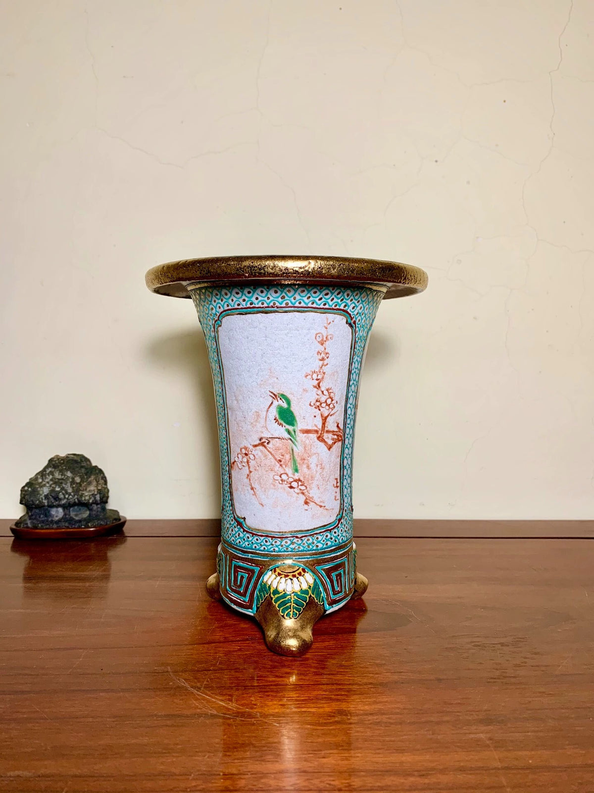A tall, flared ceramic pot with a gold rim, turquoise border, and painted bird on a light blue background.
