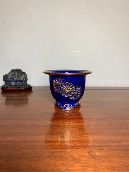 A glossy cobalt blue ceramic pot with gold floral patterns and a footed base.