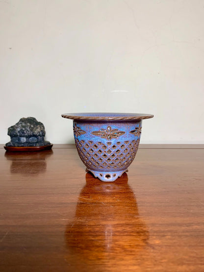 A blue glazed ceramic pot with a brown lattice pattern and floral motif, three feet.