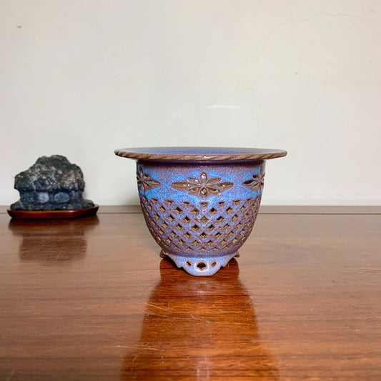 A blue glazed ceramic pot with a brown lattice pattern and floral motif, three feet.