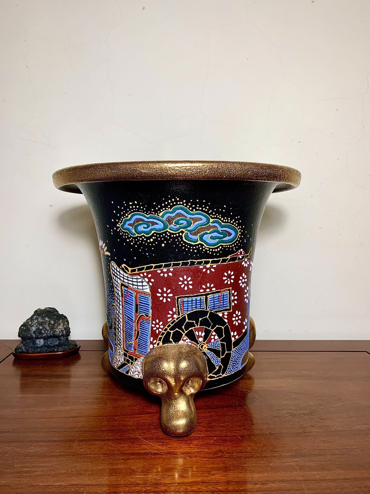 Black glazed pot with gold rim, red and blue painted scene, and gold monkey head foot.