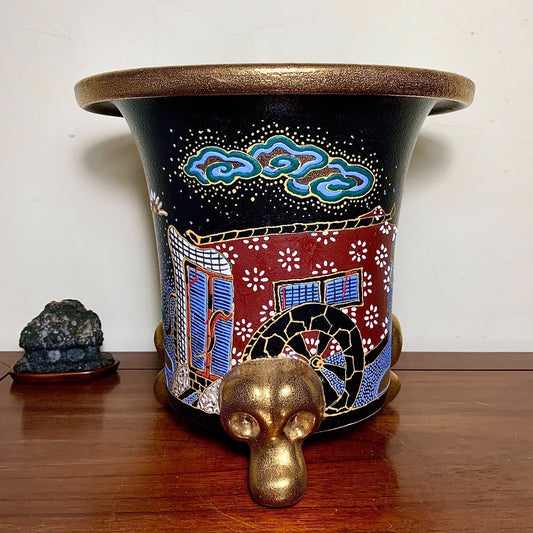 Black glazed pot with gold rim, red and blue painted scene, and gold monkey head foot.