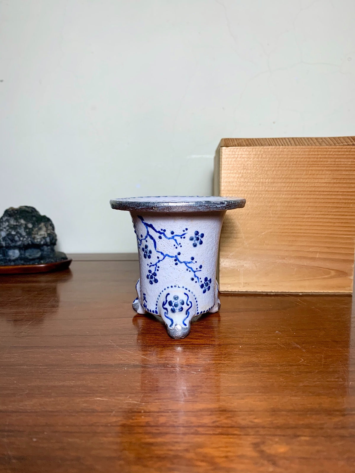 White glazed pot with blue floral pattern, three feet, dark rim.