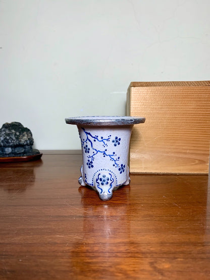 White glazed pot with blue floral pattern, three feet, dark rim.