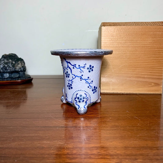White glazed pot with blue floral pattern, three feet, dark rim.