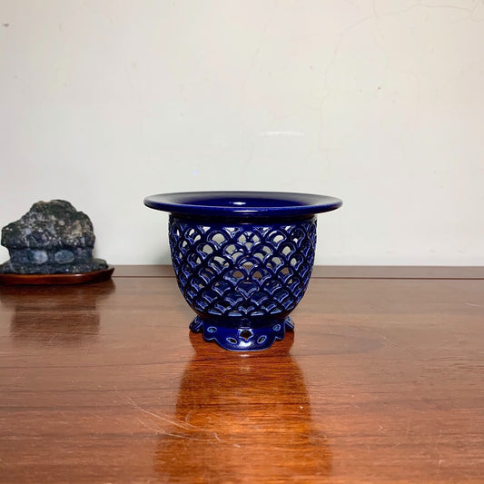 A glossy cobalt blue ceramic pot with a scalloped rim and intricate lattice pattern.