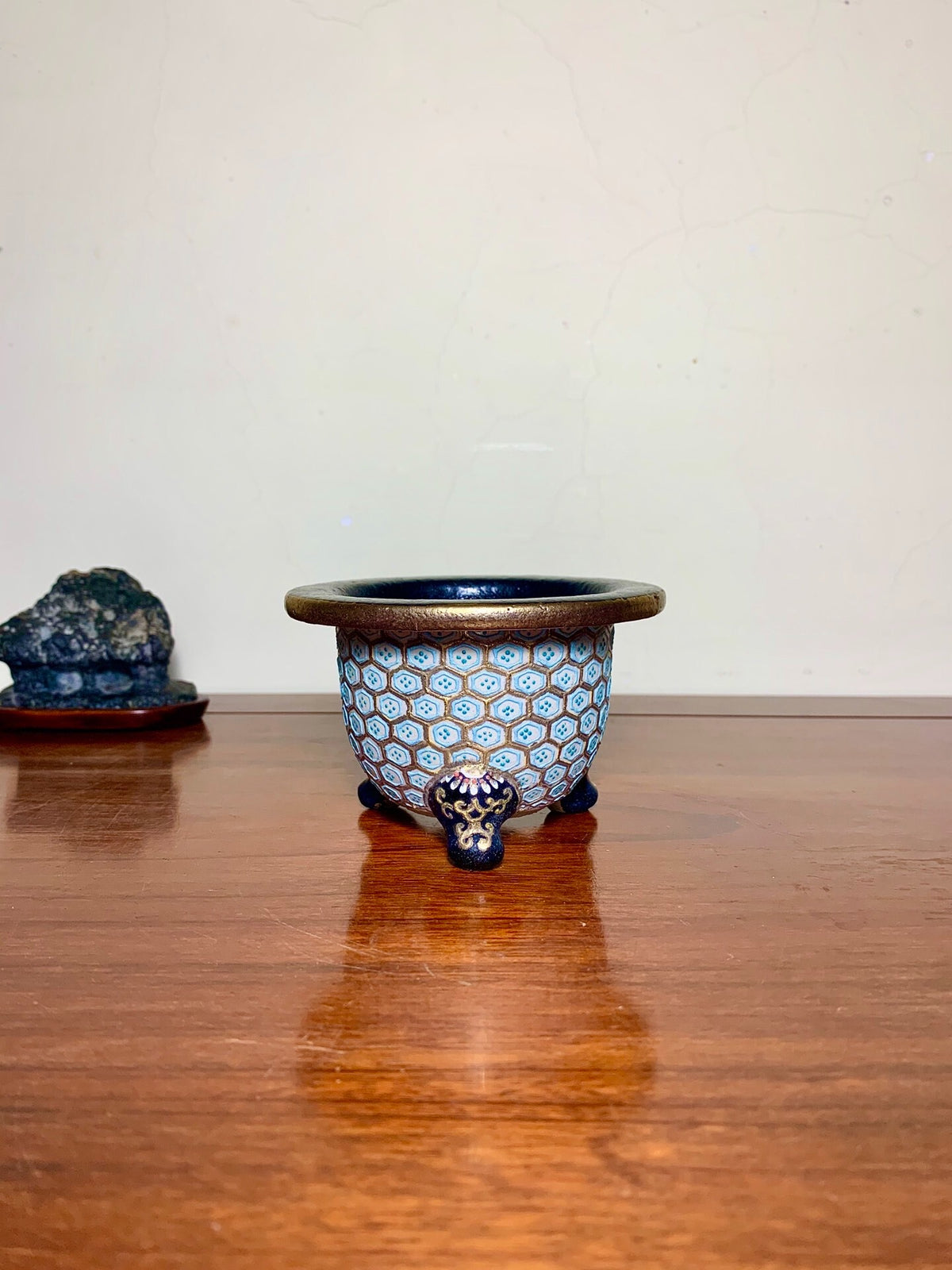 A small, round, blue-glazed pot with hexagonal patterns and three dark feet.
