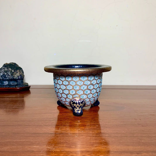 A small, round, blue-glazed pot with hexagonal patterns and three dark feet.