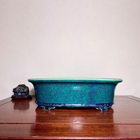 A glossy turquoise ceramic pot with speckled glaze and a green rim sits on a wooden surface.