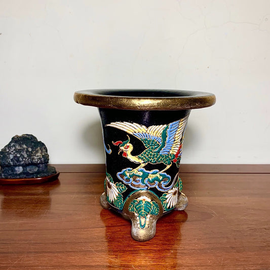 Black glazed pot with gold rim, three feet, and colorful crane decoration on clouds.