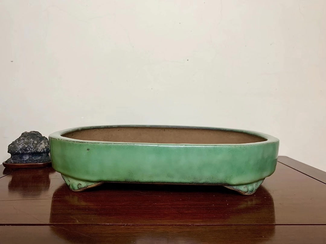 A long, low, green-glazed ceramic pot with three feet, sits on a wooden surface.