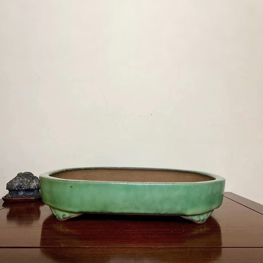 A long, low, green-glazed ceramic pot with three feet, sits on a wooden surface.