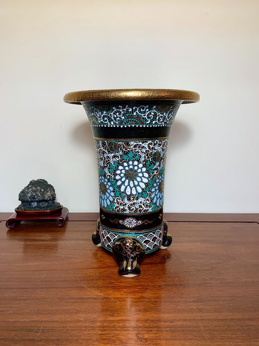A tall, flared pot with a gold rim, blue and white floral patterns, and three elephant-head feet.