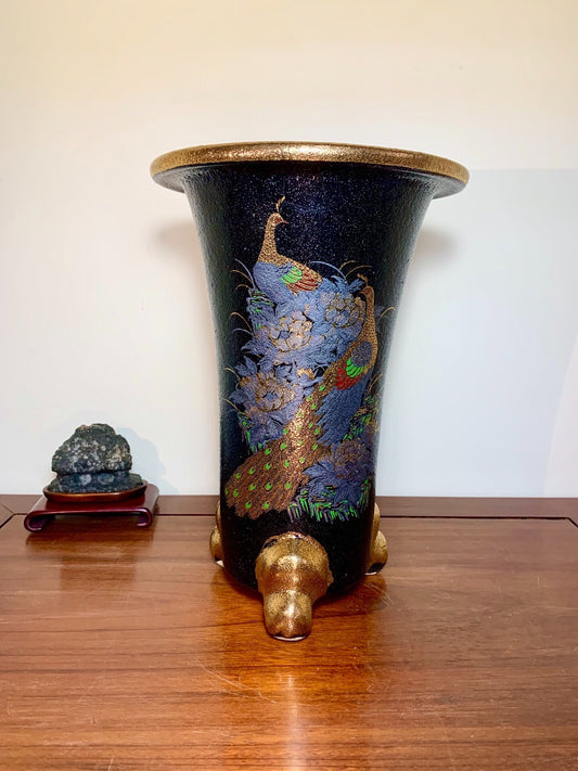 Black glazed pot with gold rim and peacock design, three gold feet.