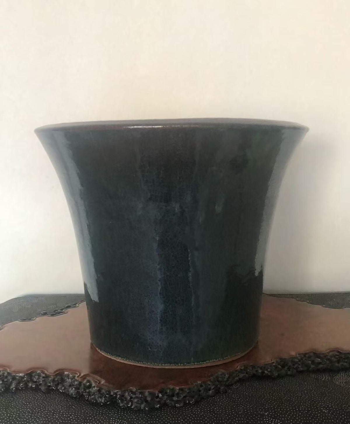 A dark, glossy ceramic pot with a flared rim sits on a wooden tray.