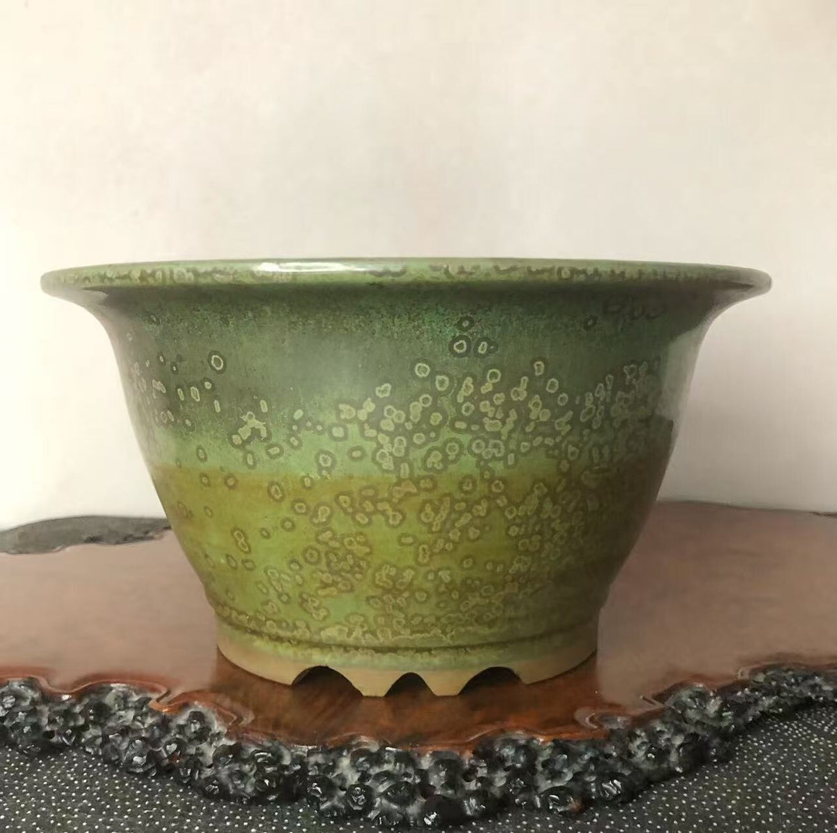 A glossy green ceramic pot with speckled patterns and a flared rim.