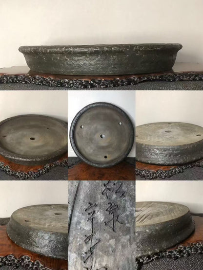 Dark grey, shallow, unglazed ceramic pot with three drainage holes and carved characters on its side.