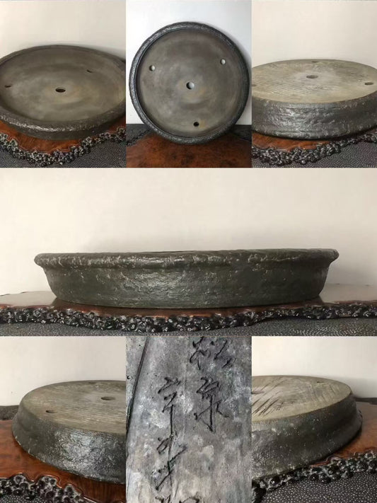 Dark grey, shallow, unglazed ceramic pot with three drainage holes and carved characters on its side.