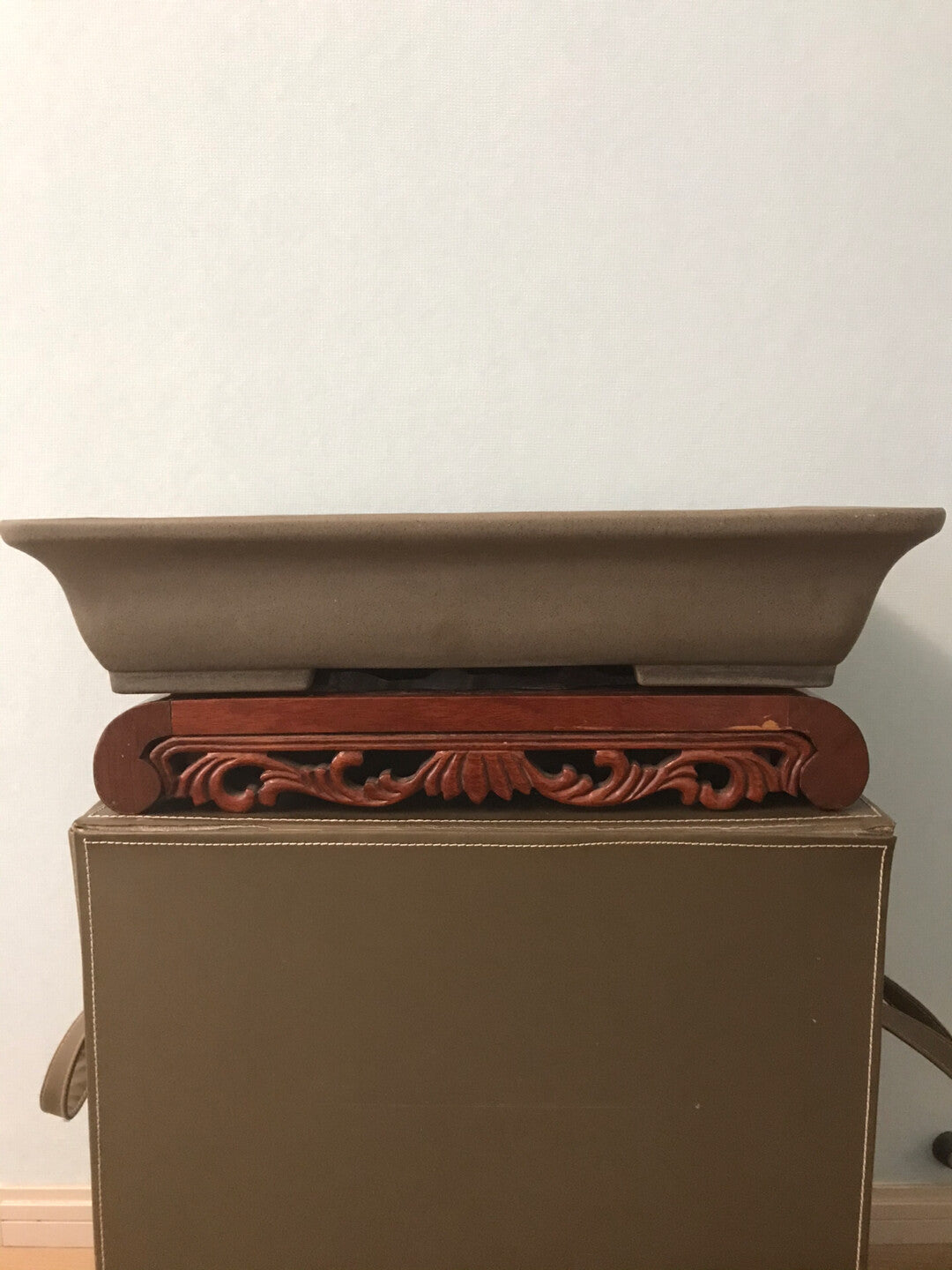 A brown glazed rectangular pot rests on an ornate wooden stand with carved floral patterns.