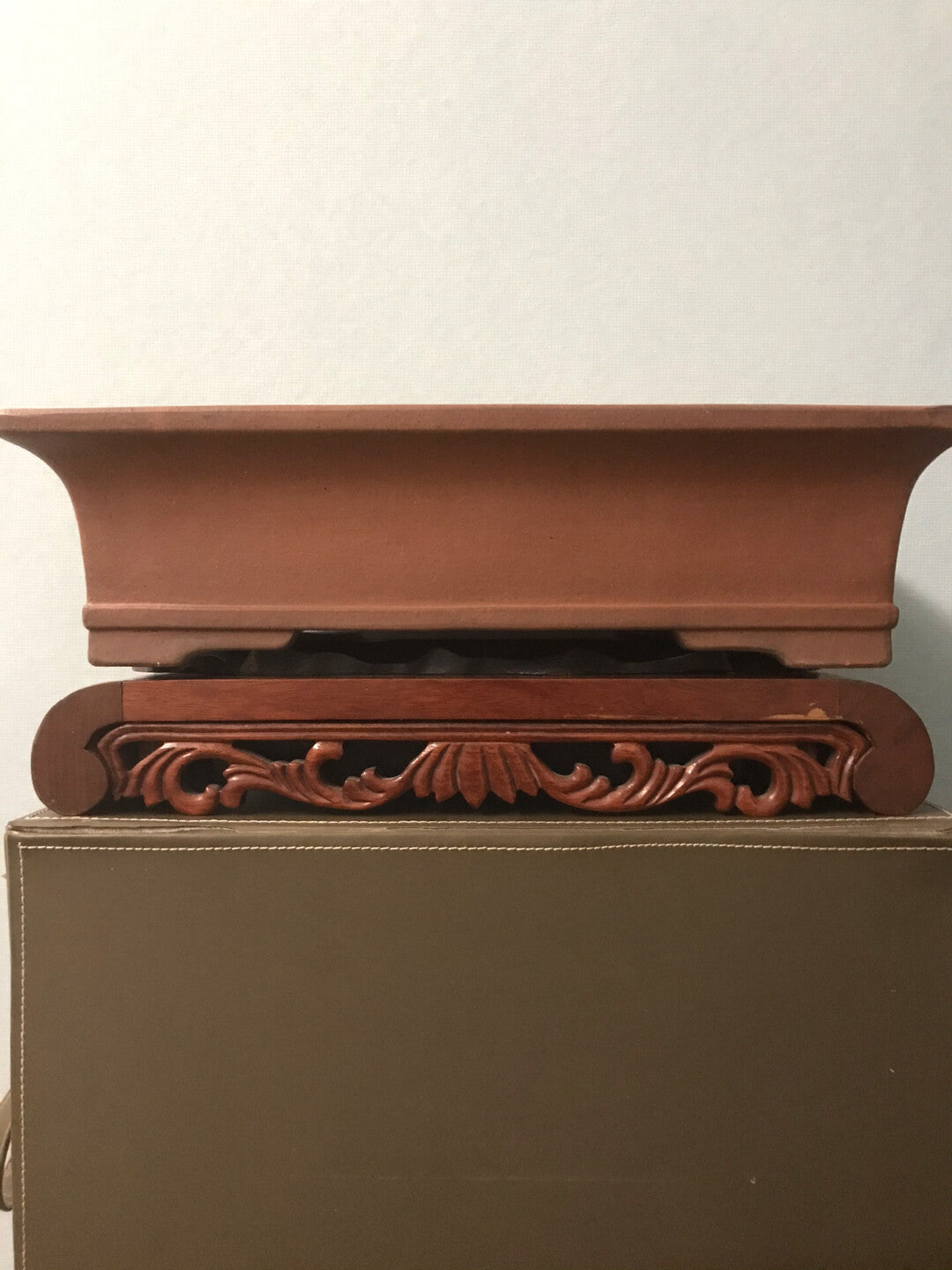 A terracotta bonsai pot with a rectangular shape and a carved wooden stand beneath it.