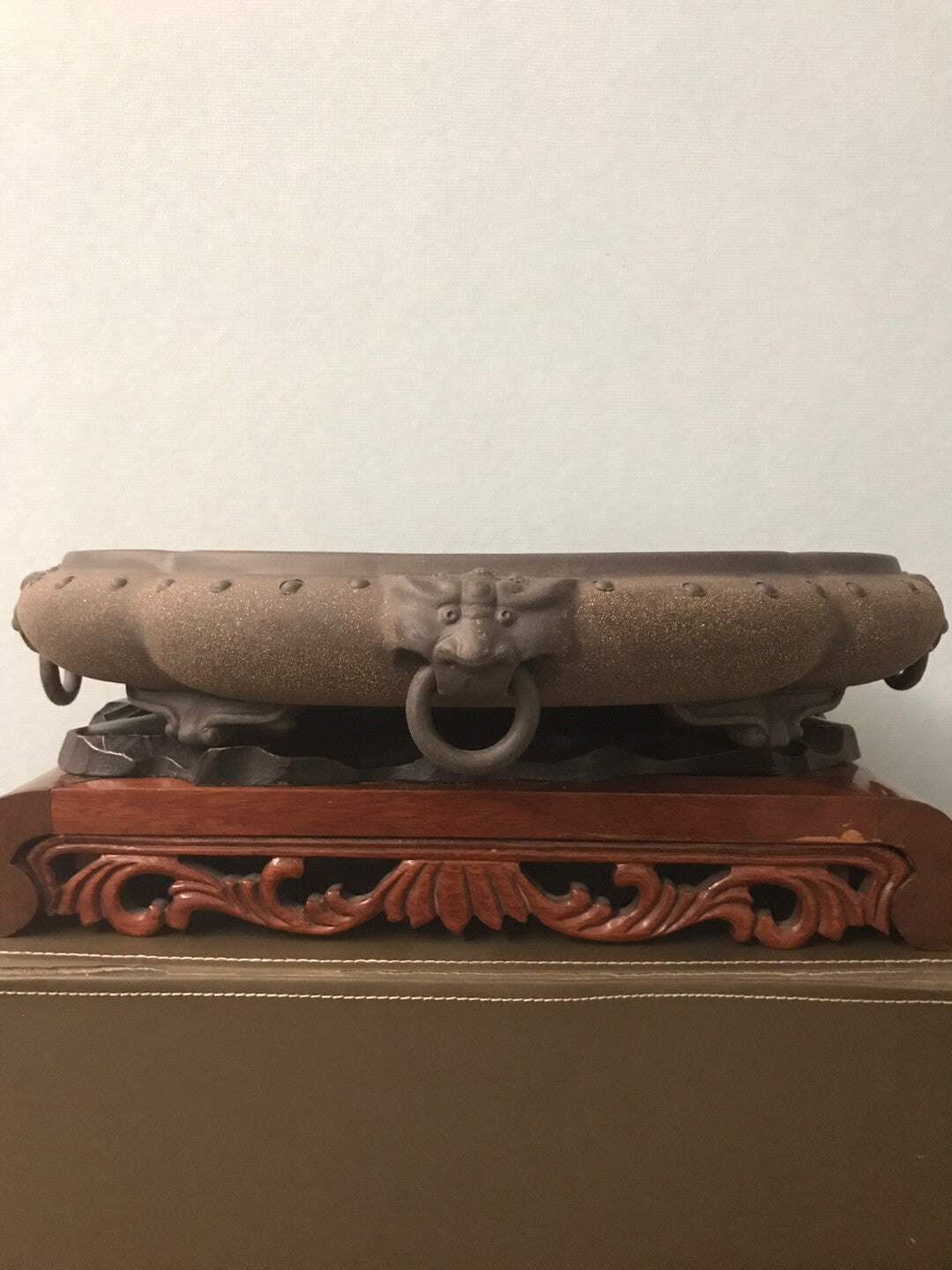 Dark brown glazed pot with lion-head ring handle, resting on carved wooden stand.