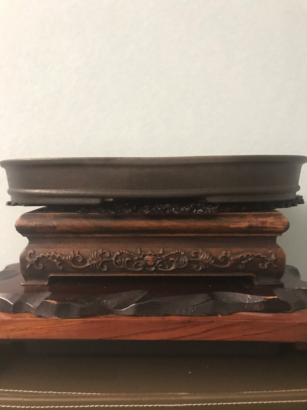 Dark brown glazed ceramic pot on ornate wooden stand with carved floral pattern.
