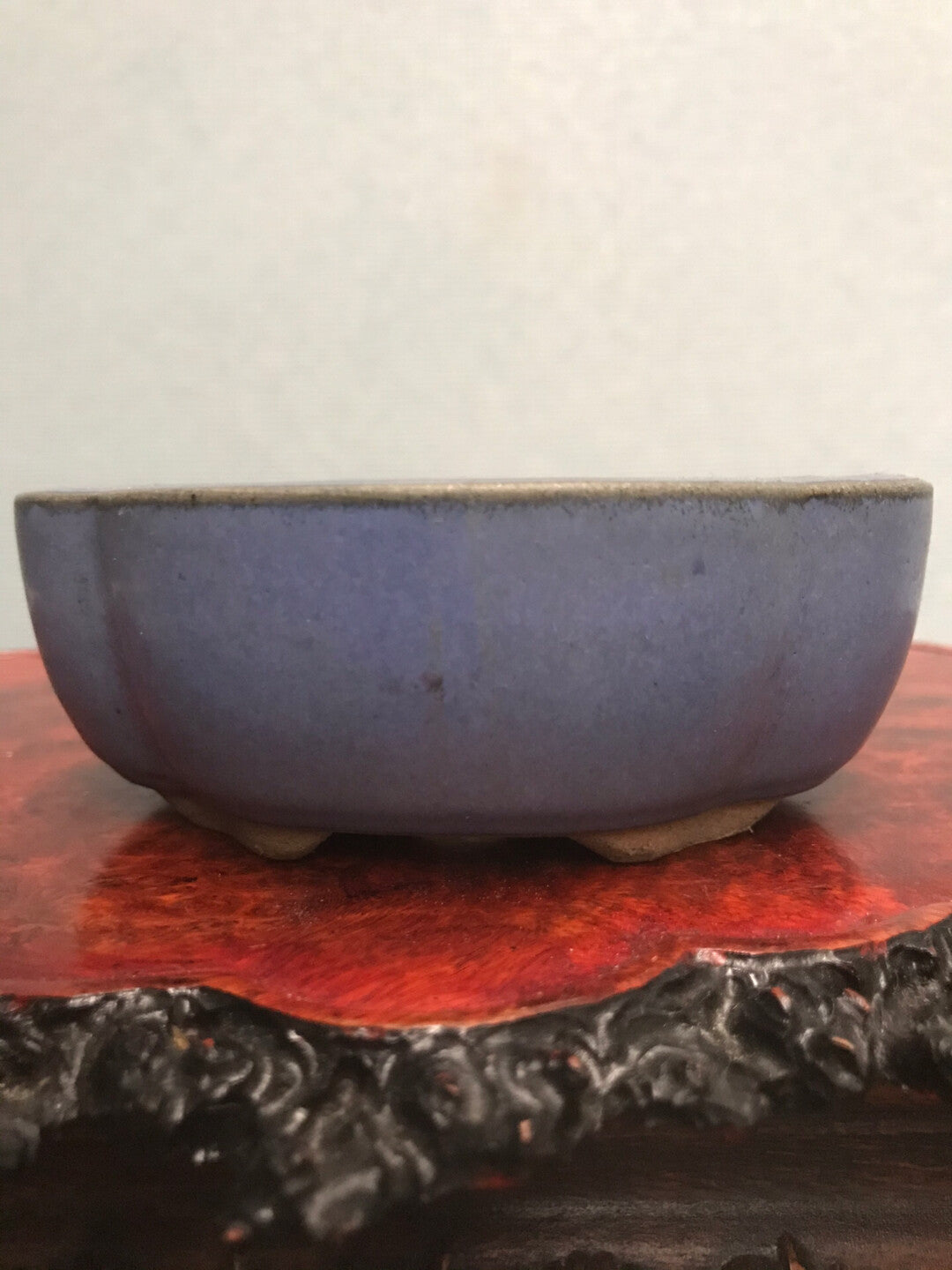 A small, deep blue glazed ceramic pot with a matte finish rests on a red wooden stand.